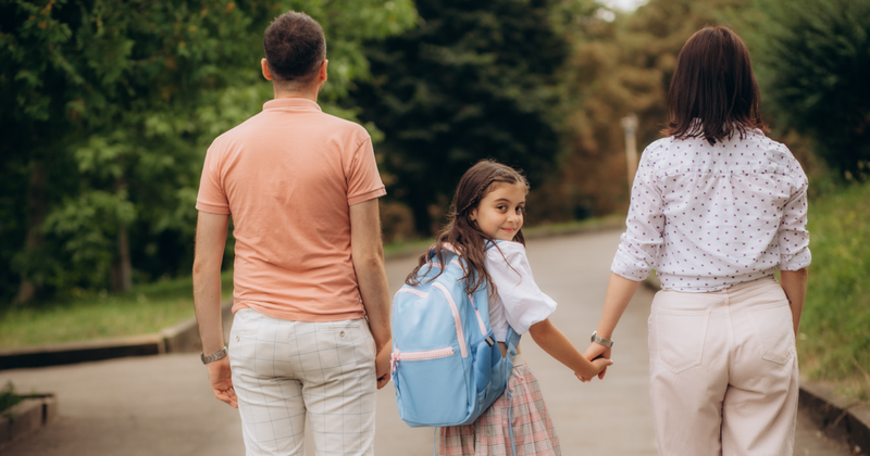 Realtor handing house keys to a family in front of a school